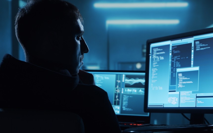 Symbolbild für einen Hacker: Ein Mann im Hoodie sitzt vor Computerbildschirmen